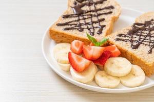 pão integral torrado com banana fresca, morango e chocolate no café da manhã foto