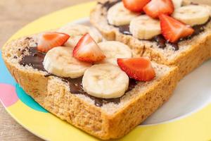 pão integral torrado com banana fresca, morango e chocolate no café da manhã foto