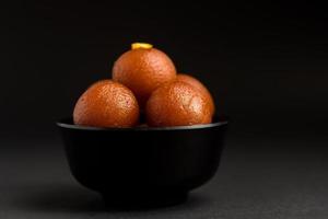 gulab jamun em tigela sobre fundo preto. sobremesa indiana ou prato doce. foto