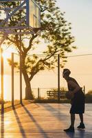 Preto homem fazendo Esportes, jogando basquetebol em nascer do sol, ativo estilo de vida, ensolarado verão manhã foto