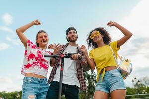 feliz jovem companhia do sorridente amigos dançando caminhando dentro rua com elétrico pontapé lambreta foto