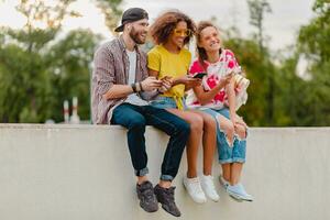 feliz jovem companhia do sorridente amigos sentado dentro parque foto