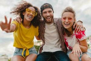 feliz jovem companhia do sorridente amigos sentado dentro parque foto