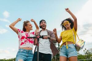 feliz jovem companhia do sorridente amigos dançando caminhando dentro rua com elétrico pontapé lambreta foto