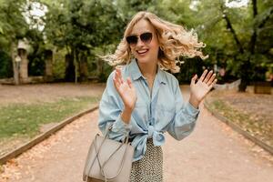 atraente loiro sorridente mulher caminhando dentro parque dentro à moda equipamento foto