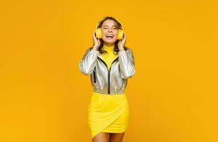 sorridente atraente mulher ouvindo para música dentro fones de ouvido em amarelo fundo foto