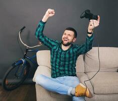 jovem hipster bonito barbudo homem sentado em sofá às lar, jogando vídeo jogos foto