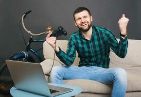 jovem hipster bonito barbudo homem sentado em sofá às lar, jogando vídeo jogos foto
