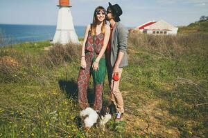 jovem à moda hipster casal dentro amor caminhando com cachorro dentro campo foto