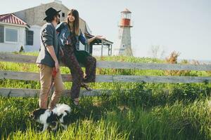 jovem à moda hipster casal dentro amor caminhando com cachorro dentro campo foto