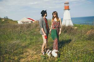 jovem à moda hipster casal dentro amor caminhando com cachorro dentro campo foto