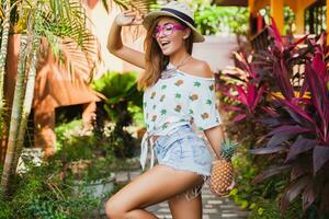 atraente sorridente mulher em período de férias segurando abacaxi foto