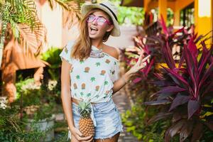 atraente sorridente mulher em período de férias segurando abacaxi foto