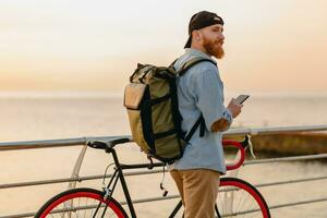 jovem barbudo homem viajando em bicicleta às pôr do sol mar foto