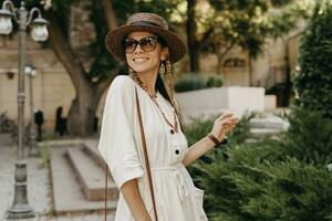 atraente mulher caminhando dentro rua em período de férias vestido dentro branco verão moda vestir foto