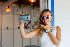 atraente mulher dentro branco vestir dentro verão cafeteria dentro oculos de sol usando telefone levando foto