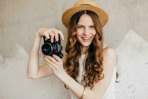 jovem bonita sorridente feliz mulher dentro Palha chapéu segurando vintage foto Câmera, grandes encaracolado cabelo