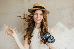 jovem bonita sorridente feliz mulher dentro Palha chapéu segurando vintage foto Câmera, grandes encaracolado cabelo