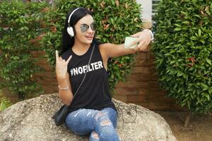 jovem à moda hipster mulher dentro Preto camiseta, jeans, ouvindo para música em fones de ouvido foto