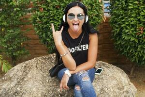 jovem à moda hipster mulher dentro Preto camiseta, jeans, ouvindo para música em fones de ouvido foto