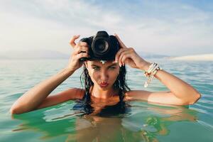 lindo mulher, bronzeada pele, Preto bikini roupa de banho, em pé dentro azul água foto