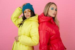 dois atraente à moda mulheres posando em Rosa fundo dentro colorida inverno baixa Jaqueta do vermelho e amarelo cor, caloroso roupas moda tendência foto