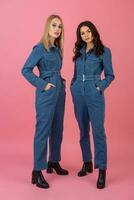 dois animado atraente menina amigos ativo mulheres posando em Rosa fundo dentro jeans No geral tendo Diversão juntos moda tendência foto