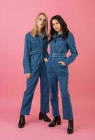 dois animado atraente menina amigos ativo mulheres posando em Rosa fundo dentro jeans No geral tendo Diversão juntos moda tendência foto