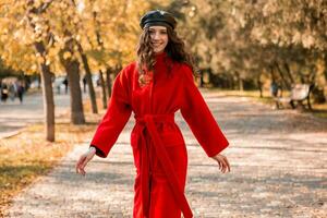 atraente à moda mulher caminhando dentro parque vestido dentro caloroso vermelho casaco foto