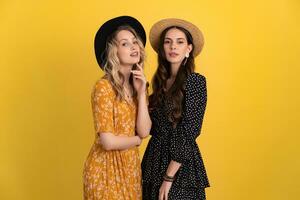 lindo mulheres amigos juntos isolado em amarelo fundo dentro Preto e amarelo vestir e chapéu foto