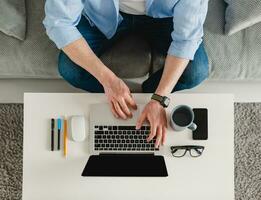 Visão em mesa local de trabalho fechar-se homem mãos às casa trabalhando digitando em computador portátil conectados foto
