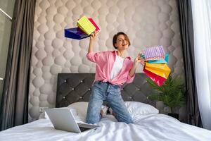 bonita feliz mulher pulando em cama às compras para casa conectados foto