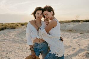 dois jovem mulheres tendo Diversão em a pôr do sol de praia foto