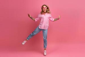 loiro bonita mulher dentro Rosa camisa e jeans sorridente pulando foto