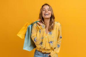 lindo atraente sorridente mulher dentro amarelo camisa e jeans segurando compras bolsas foto