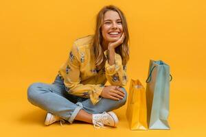 lindo atraente sorridente mulher dentro amarelo camisa e jeans com compras bolsas foto