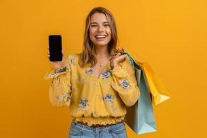lindo atraente sorridente mulher dentro amarelo camisa e jeans segurando compras bolsas foto