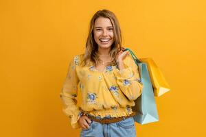 lindo atraente sorridente mulher dentro amarelo camisa e jeans segurando compras bolsas foto