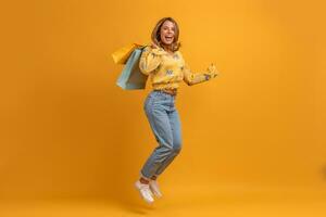 lindo atraente sorridente mulher dentro amarelo camisa e jeans com compras bolsas foto