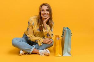 lindo atraente sorridente mulher dentro amarelo camisa e jeans com compras bolsas foto