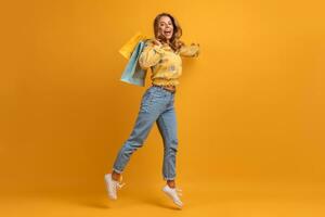 lindo atraente sorridente mulher dentro amarelo camisa e jeans com compras bolsas foto