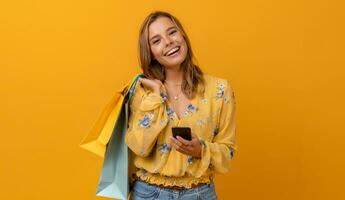 lindo atraente sorridente mulher dentro amarelo camisa e jeans segurando compras bolsas foto