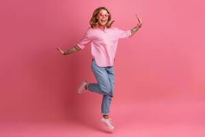 loiro bonita mulher dentro Rosa camisa e jeans sorridente pulando foto