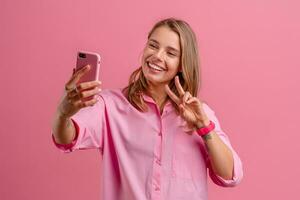 loiro bonita mulher dentro Rosa camisa sorridente segurando segurando usando Smartphone foto