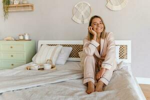 bonita sorridente mulher relaxante às casa em cama dentro manhã dentro pijamas foto