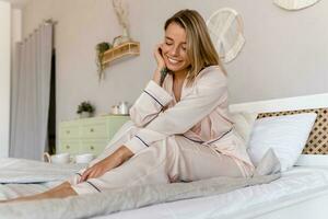 bonita sorridente mulher relaxante às casa em cama dentro manhã dentro pijamas foto