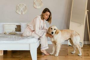 bonita sorridente mulher relaxante às casa em cama dentro manhã dentro pijamas com cachorro foto