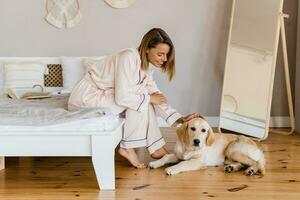 bonita sorridente mulher relaxante às casa em cama dentro manhã dentro pijamas com cachorro foto