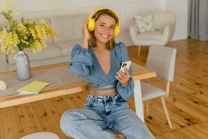 jovem bonita à moda sorridente mulher relaxante às casa ouvindo para música em fones de ouvido foto