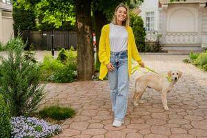 feliz sorridente mulher dentro amarelo suéter caminhando às dela casa com uma cachorro dourado retriever foto